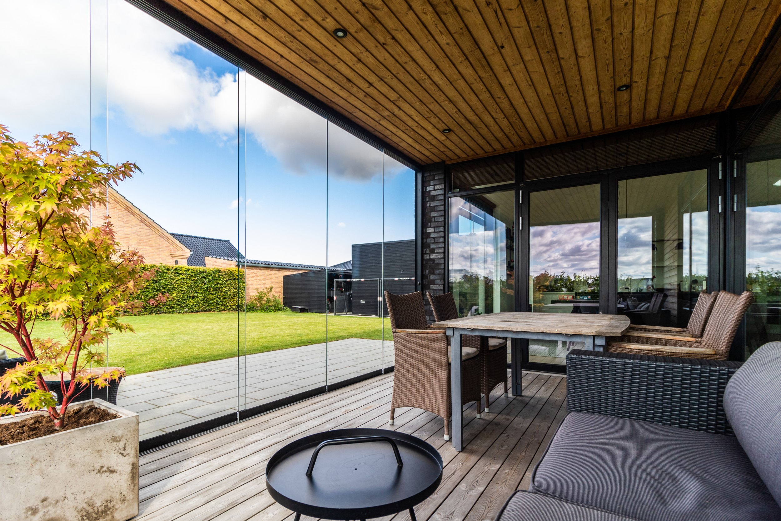 En glasinddækning af en overdækket terrasse, hvor spisebord og sofaområde kigger ud på grøn have | VICA Danmark