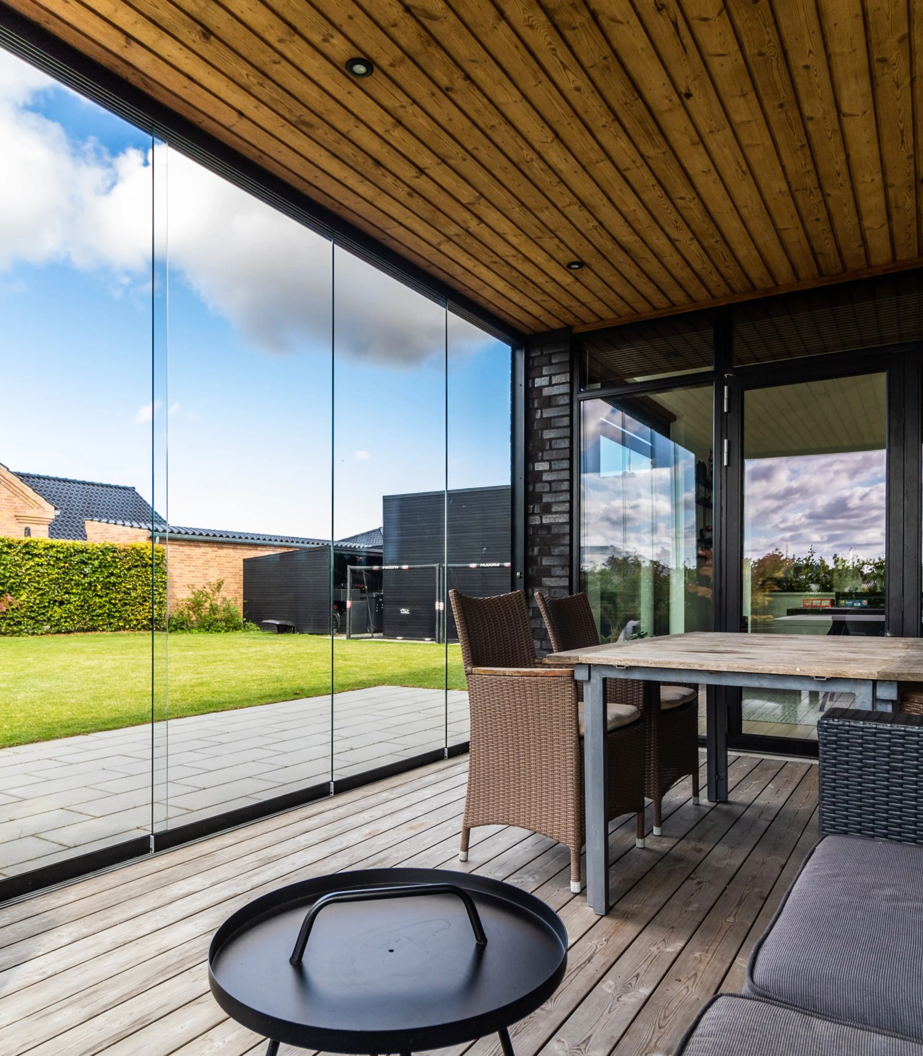 En glasinddækning af en overdækket terrasse, hvor spisebord og sofaområde kigger ud på grøn have | VICA Danmark